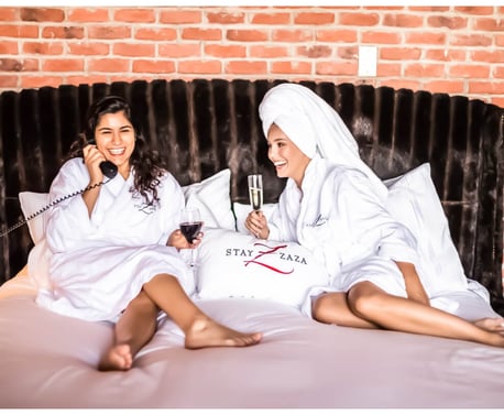 Two friends laying in bed drinking wine
